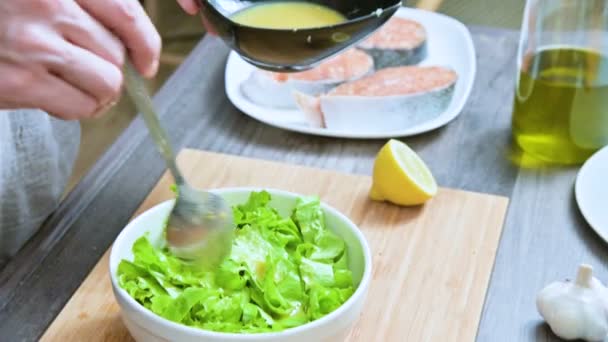 Gros plan des mains féminines dans une cuisine maison sont ajoutés à une sauce salade de feuilles végétarienne et mélangés avec une cuillère sur une planche à découper en bois — Video