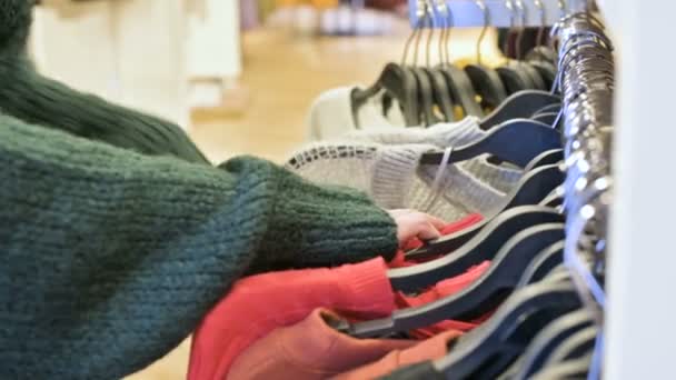 Närbild av en flickor hand i en butik att välja kläder som hänger på galgar till salu — Stockvideo
