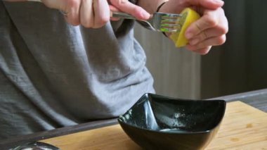 Sosu yapmak için siyah bir kapta limon kullanarak bir çatal ile yakın çekim kız sıkıyor