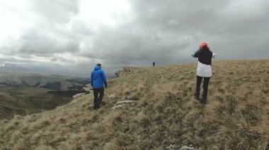 Turistler üç kişilik bir grubun dağlarda yüksek Plato kenarına bulutlu havalarda yürümek. Ağır çekim. 4k Uhd