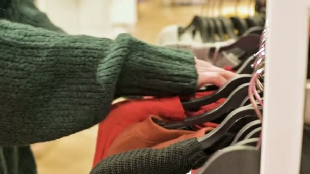 Γκρο πλαν ενός χεριού κορίτσια σε ένα κατάστημα που επιλέγουν ρούχα που κρέμονται στις κρεμάστρες προς πώληση — Αρχείο Βίντεο