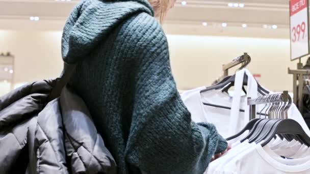 Close-up de uma mão de meninas em uma loja escolhendo roupas penduradas em cabides para venda — Vídeo de Stock