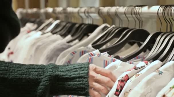 Close-up de uma mão de meninas em uma loja escolhendo roupas penduradas em cabides para venda — Vídeo de Stock