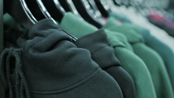 Primer plano de sudaderas con capucha multicolor en perchas en una tienda de ropa — Vídeos de Stock