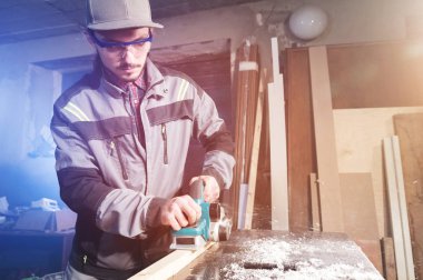 Genç sakallı bir elektrikli uçak talaş emme ile çalışan bir marangoz. Tesviye ve ahşap çubukları zımpara