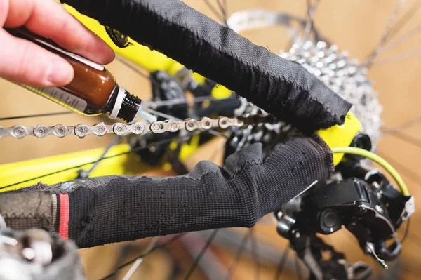 Nahaufnahme einer Männerhand, angeführt von Meistern, schmiert die Fahrradkette eines Mountainbikes mit einem speziellen Schmiermittel in der heimischen Werkstatt — Stockfoto