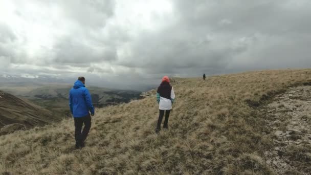 Un grupo de turistas tres personas caminan en clima nublado en el borde de la meseta alta en las montañas. En cámara lenta. 4K UHD — Vídeo de stock