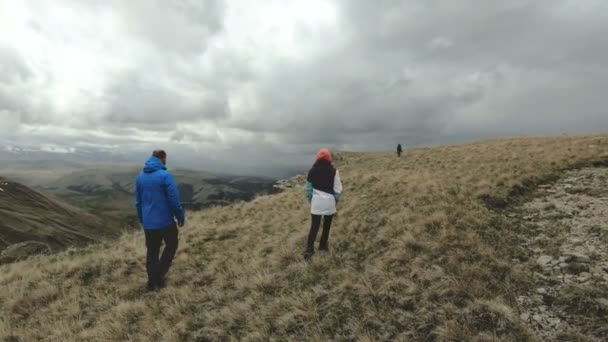 A group of tourists three people walk in cloudy weather on the edge of the plateau high in the mountains. Slow motion. 4K UHD — Stock Video