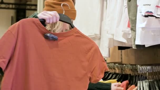 Närbild av en flickor hand i en butik att välja kläder som hänger på galgar till salu — Stockvideo