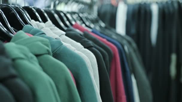 Primer plano de sudaderas con capucha multicolor en perchas en una tienda de ropa — Vídeos de Stock