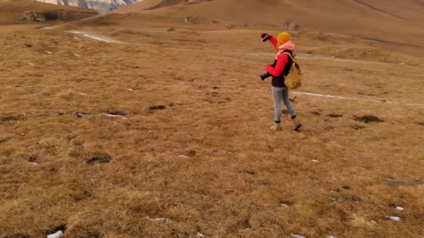 Hava görünümü. Bir gezgin kız onun etrafında bir kamera ile boyun ve yamaç arka plan dağlar ve bulutlu bir plato günbatımında yürüyor. Kız resimleri telefonda alır. — Stok video