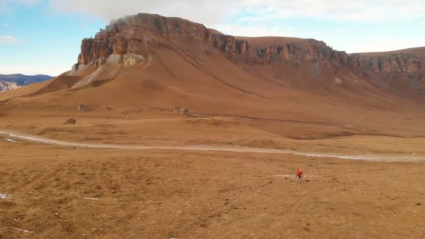 Vue aérienne. Une voyageuse avec une caméra autour du cou et marche le long de la pente un fond de montagnes et un plateau avec des nuages au coucher du soleil. La fille prend des photos au téléphone — Video