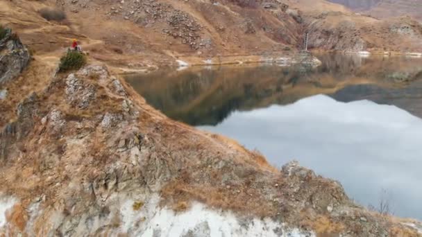Vista aérea de una chica sentada en una roca en una orilla del lago que mira a la naturaleza — Vídeo de stock