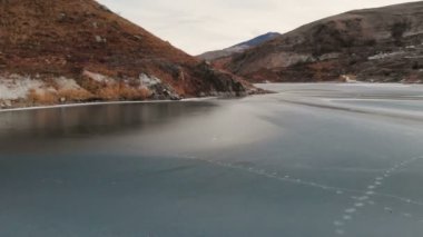 Mavi saatte güneş battıktan sonra Kafkas Dağları ile çevrili kışın donmuş bir gölün üzerinde düşük uçuş havadan görünümü