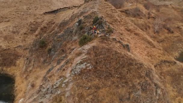 Vista aérea de una niña sentada en una roca de un promontorio en la orilla del lago vierte té de un termo — Vídeos de Stock