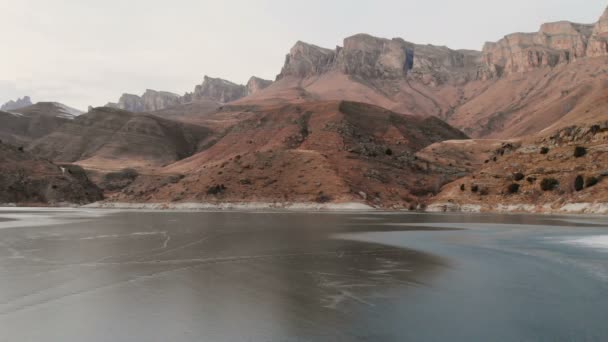 Vista aérea de um voo baixo sobre um lago congelado no inverno cercado pelas montanhas do Cáucaso após o pôr do sol na hora azul — Vídeo de Stock