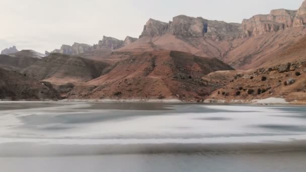 Vista aérea de un vuelo bajo sobre un lago congelado en invierno rodeado por las montañas del Cáucaso después del atardecer a la hora azul — Vídeo de stock