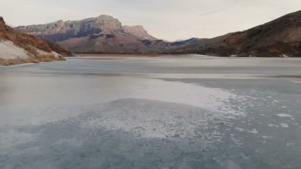 Vista aérea de un vuelo bajo sobre un lago congelado en invierno rodeado por las montañas del Cáucaso después del atardecer a la hora azul — Vídeo de stock