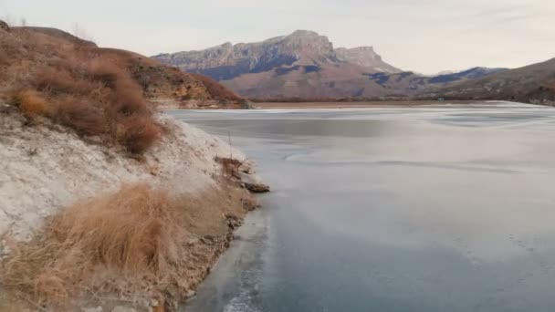 Vista aérea de un vuelo bajo sobre un lago congelado en invierno rodeado por las montañas del Cáucaso después del atardecer a la hora azul — Vídeo de stock