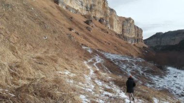 Kız turistik bir aşağı ceket ve şapka yol boyunca erken kayalık bir geçit kışın içeri girer. Sarı çim ve güneşli bir günde kar parçaları. Havadan görünümü