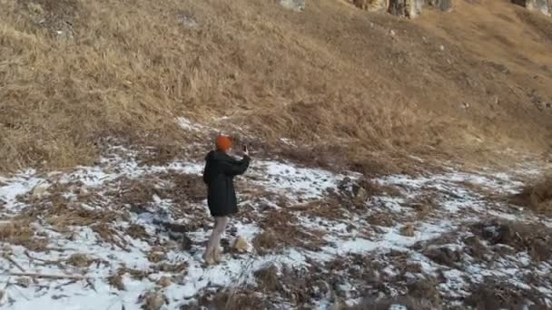 Touristinnen in Daunenjacke und Mütze gehen im frühen Winter den Weg entlang. macht ein Foto mit dem Smartphone. Luftbild — Stockvideo