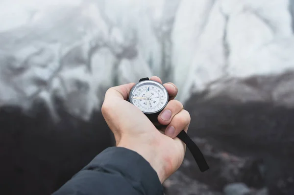 Una vista en primera persona de una mano de hombre sosteniendo una brújula magnética sobre un fondo de glaciar agrietado espolvoreado con polvo volcánico. El concepto de encontrar destinos y viajar — Foto de Stock