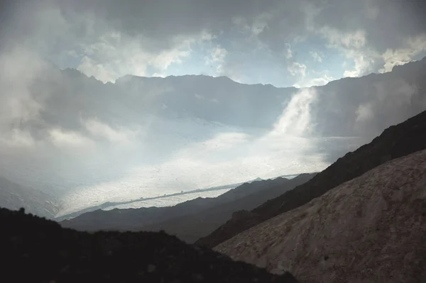 Yüksek dağ eğim Kafkas Dağları bulutlar penceresinde zemin karşı kırık buzul çamurlu volkanik eğimli dağ manzarası. Kuzey Kafkasya buzulların — Stok fotoğraf