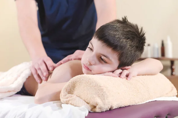 Zbliżenie małego chłopca rozluźnia z masażu leczniczego. Mężczyzna masażysta sprawia, że masaż leczniczy pleców dziecka — Zdjęcie stockowe