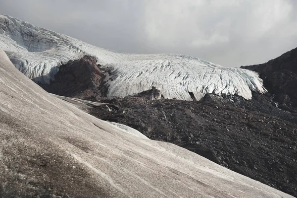 Paesaggio montano polveroso pendio vulcanico sporco con ghiacciaio fuso incrinato. Riscaldamento globale. Ghiacciai del Caucaso settentrionale — Foto Stock