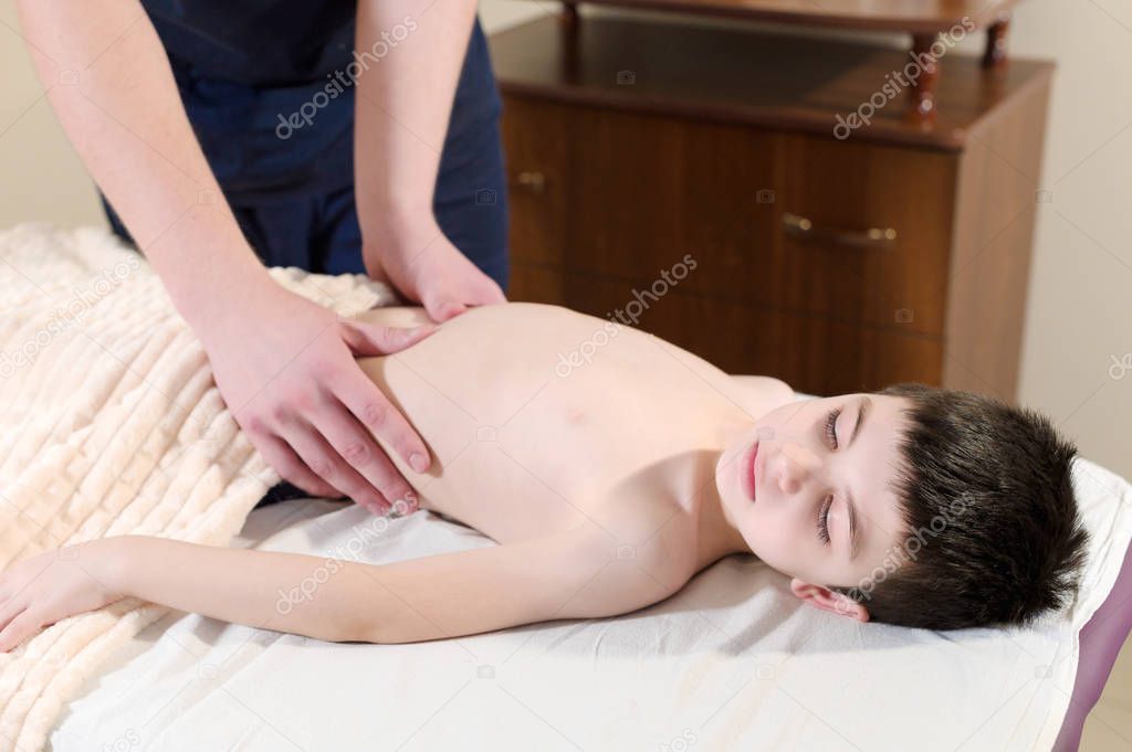 A little boy at the reception at a professional masseuse. Male manual worker gives massage to the front of the child
