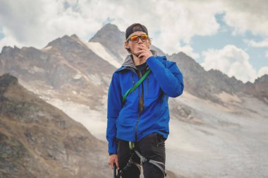 Bir profesyonel rehber-dağcı bir şapka ve güneş gözlüğü elinde bir sigara gökyüzü ve Kafkasya karla kaplı dağlar karşı bir buz balta ile portresi. Sigara sorun