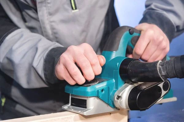 Close-up de uma mão carpinteiros trabalhando com um plano elétrico com sucção de serragem. Nivelamento e lixamento barras de madeira — Fotografia de Stock