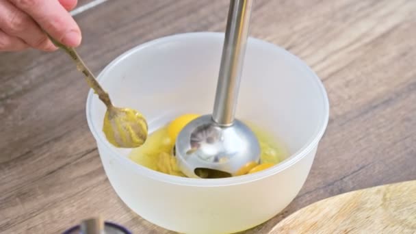 Close-up of hands. The girl at the home kitchen beats chicken eggs in a plastic bowl submersible electro blender — Stock Video