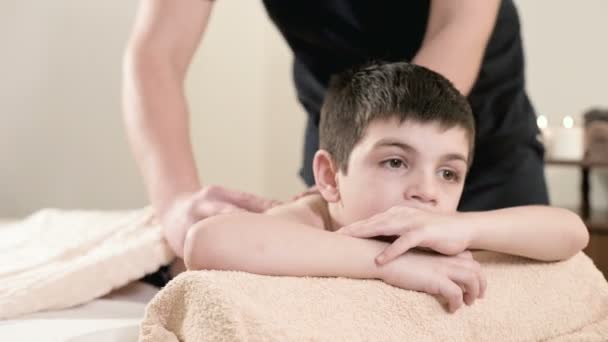 男性理疗师按摩师对躺在按摩床上的小男孩进行治疗放松按摩。肩部和背部按摩 — 图库视频影像