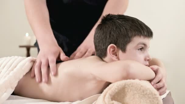 Un masseur kinésithérapeute masculin fait un massage relaxant curatif à un petit garçon allongé sur un lit de massage. Massage d'épaule et de dos — Video