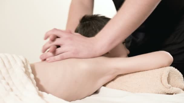 A male physiotherapist masseur makes a healing relaxing massage to a little smiling boy lying on a massage bed. Massage of the loin and back — Stock Video