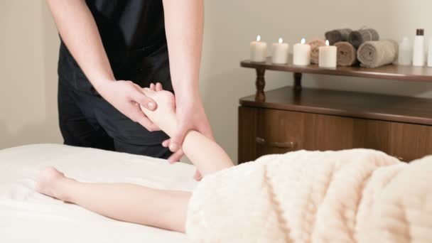 Homem fisioterapeuta massagista fazendo uma cura relaxante massagem nos pés para uma pequena criança deitada em uma cama de massagem — Vídeo de Stock