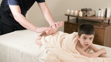Bir erkek fizyoterapist masör bir rahatlatıcı masaj ve küçük bir çocuk bir masaj yatakta yatarken germe şifa yapar. Tendon ve kas germe