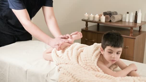 A férfi fizioterapeuta-masszőr teszi egy gyógyító, relaxáló masszázs, és a nyújtás egy kisfiú, egy masszázs ágyon. Stretching az inak és izmok — Stock videók