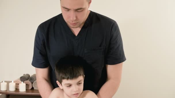 Giovane massaggiatore fisioterapista maschile che fa stretching terapeutico della schiena e della colonna vertebrale per un bambino piccolo in una sala massaggi — Video Stock