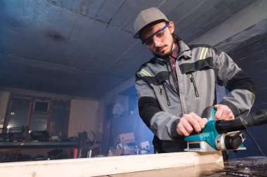 Elektrik düzlemin bir ev ahşap atölyesinde çalışan genç bir marangoz portresi. Bir iş fikri ve bir ağaç işleme başlangıç kavramı. Geniş açı