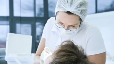 Gözlük maskesi ve beyaz şapkalı kadın diş hekimi Doktor hastanın ağız boşluğu inceliyor. Diş hekimi çalışma