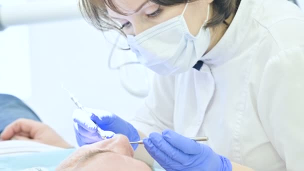 Primer plano de una mujer dentista examinando la cavidad oral de un paciente masculino a la edad. Trabajo profesional clave de un dentista en la clínica dental — Vídeos de Stock