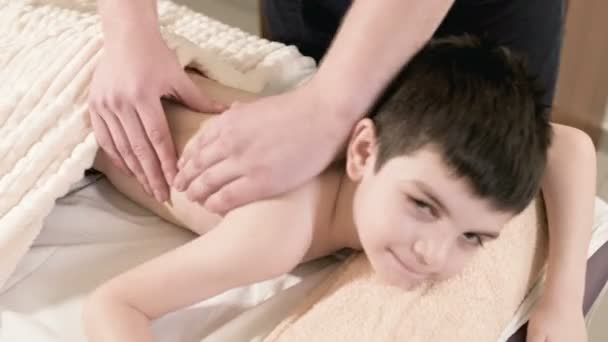 Der männliche Physiotherapeut aus nächster Nähe massiert einen kleinen Jungen, der auf einem Massagebett liegt, mit einer heilenden Entspannungsmassage. Rückenmassage — Stockvideo