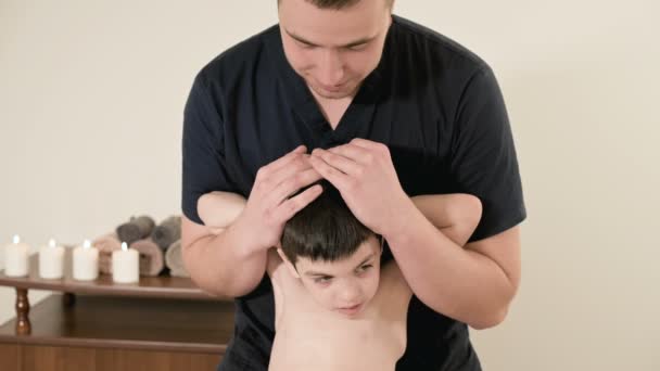 Joven masajista fisioterapeuta masculino haciendo estiramiento terapéutico de la espalda y la columna vertebral a un niño pequeño en una sala de masajes — Vídeo de stock