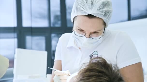 Vrouw tandarts arts in glazen masker en witte GLB onderzoekt de mondholte van de patiënt. Tandartsen werken — Stockvideo