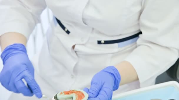 Γκρο πλαν του χεριού της οδοντιατρικής αναμειγνύονται συστατικά για ένα σύνθετο προμορφωμάτων για την αφαίρεση της φόρμας από το σαγόνι και το δάγκωμα του ασθενούς — Αρχείο Βίντεο