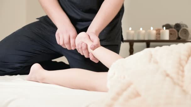 Homem fisioterapeuta massagista fazendo uma cura relaxante massagem nos pés para uma pequena criança deitada em uma cama de massagem — Vídeo de Stock