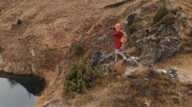 Havadan görünümü onun Dslr fotoğraf makinesi manzara fotoğrafları bir göl kıyısında bir kayanın üzerinde duran bir kız. Seyahat videoları