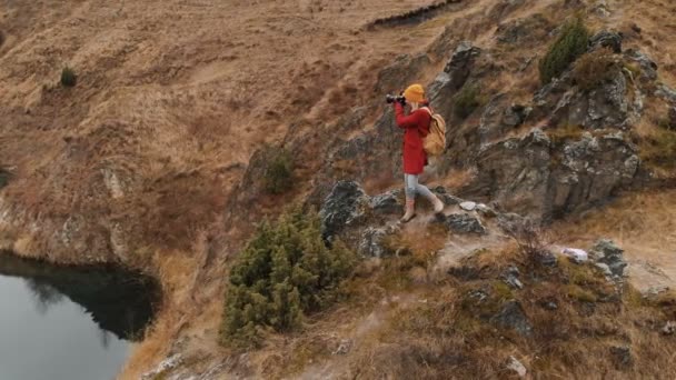 Luchtfoto van een meisje staande op een rots aan de oever van een meer, foto's van het landschap op haar Dslr camera. Travel Video — Stockvideo